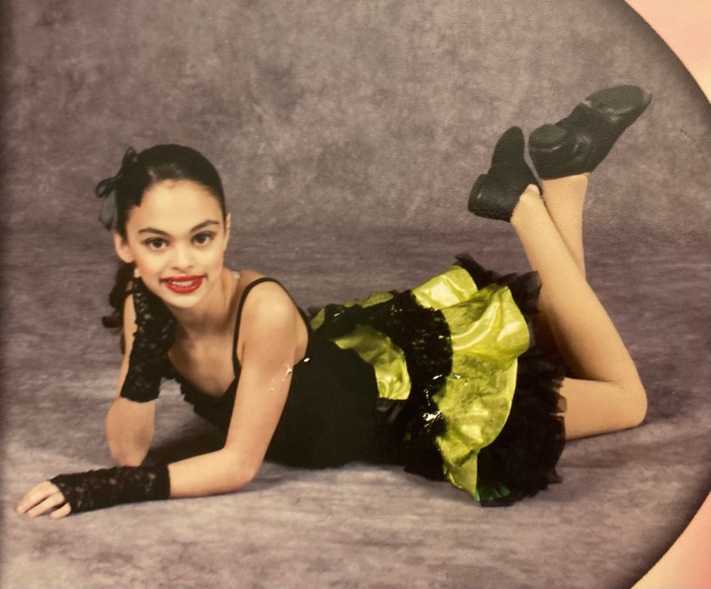 Younger me in a dance costume, black and green dress with a black bow.